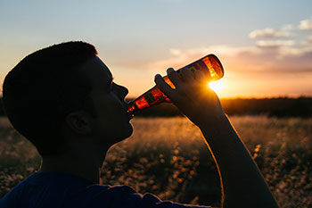 A young man drinking a beer outdoors.