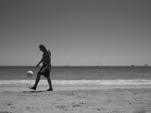 Black and white image of a man kicking a ball on the beach