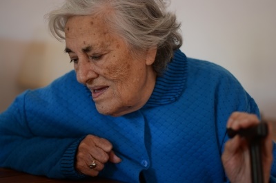 Elderly woman sitting down, looking down, holding a cane