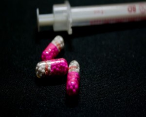 Three pills and a needle against a black background