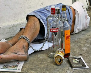 Drunk man laying down in the street with ankle chained to liquor bottles