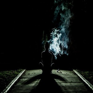 Woman's silhouette sitting on the ground smoking in pitch black