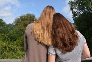 Two girls standing close with their heads together, outside