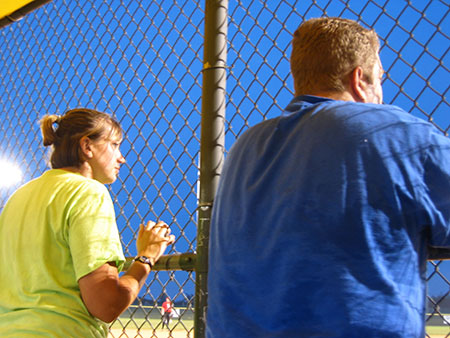 man and woman watching a baseball game through a fence