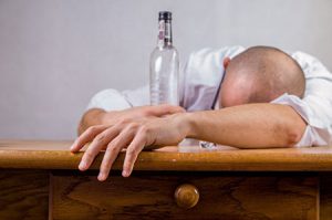 Man with a bottle of alcohol leans over a table.