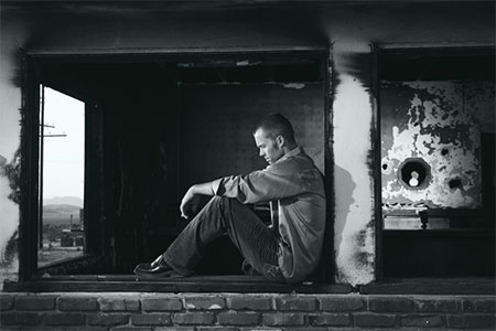 Man sitting in a run down building window suffering from addiction
