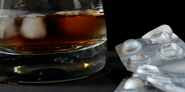 Glass of alcohol next to pack of pills against black background