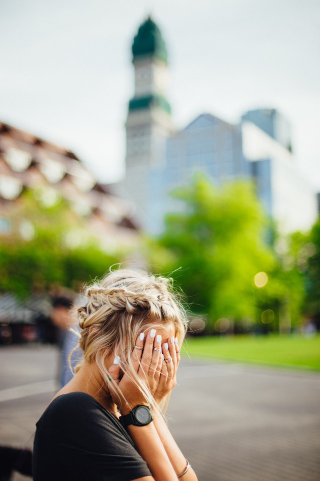 young woman covering her face with both hands in shame against blurry background