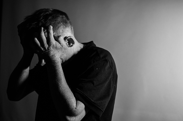 Black and white image of depressed man holding head in both hands