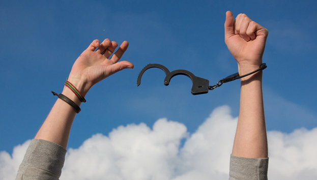 Person's hands up in the sky displaying unlocked handcuffs representing freedom