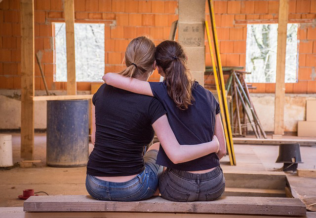 Two hard-working women sitting next to each other on wood plank in relieved embrace
