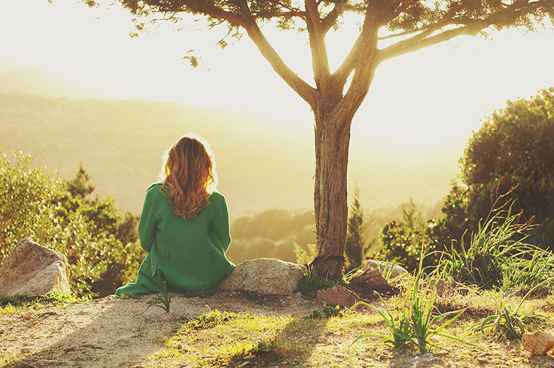 Woman sitting by tree staring off into nature