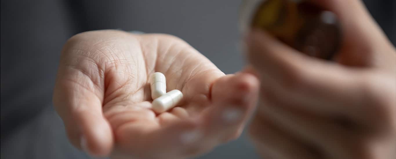 A close up of a young woman holding pills in her left hand.