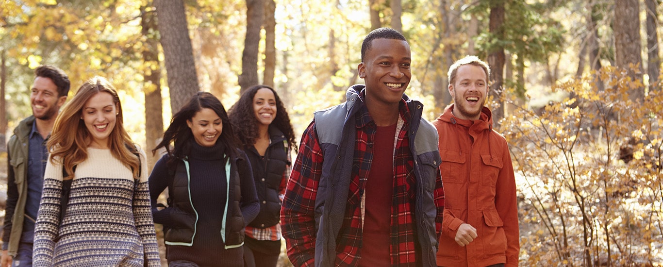 A group of young men and women smile as they hike along a forest trail.