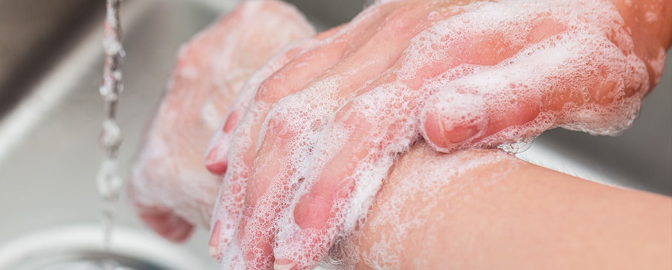 Close up of soapy hands over a kitchen sink with the water running.