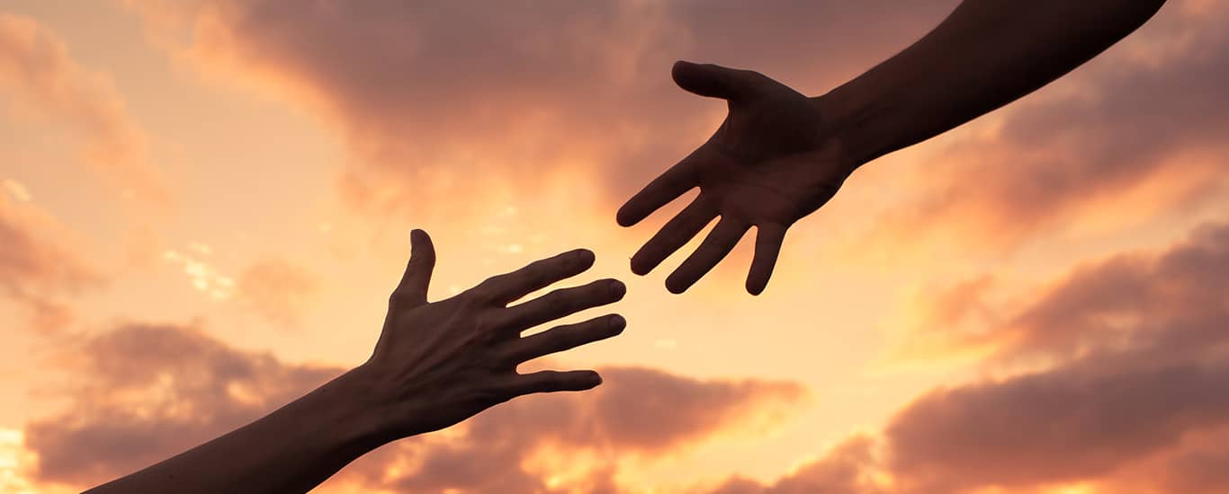 Two hands reaching for each other outside at sunset
