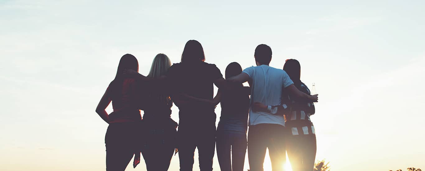 Group of people standing looking at a sunset after a group hug.
