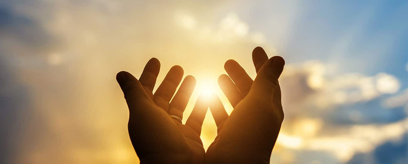 A pair of hands reaching towards the sun in worship.