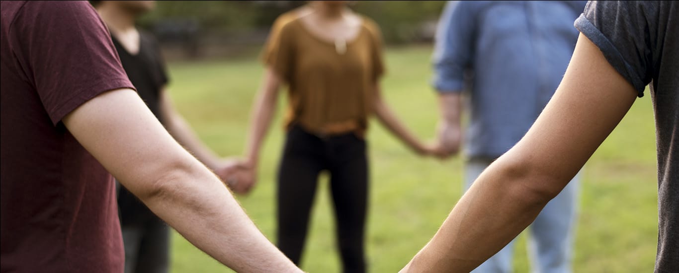 Diverse group of people holding hands in a circle in a park.