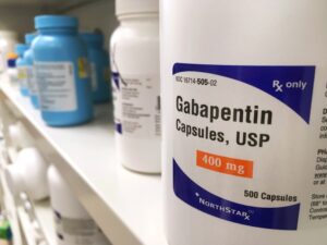 A closeup image of a Gabapentin pill bottle next to other medications on a pharmacy shelf. 