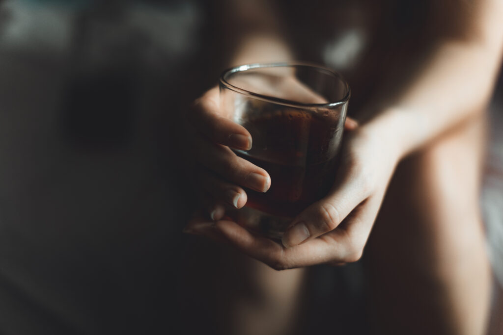 A closeup image of a glass of alcohol in a woman’s hands.