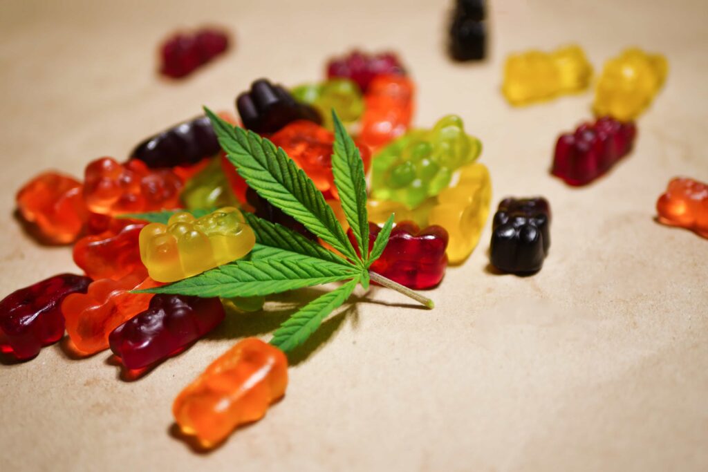 A handful of cannabis-infused gummy bears in various colors next to a marijuana leaf.